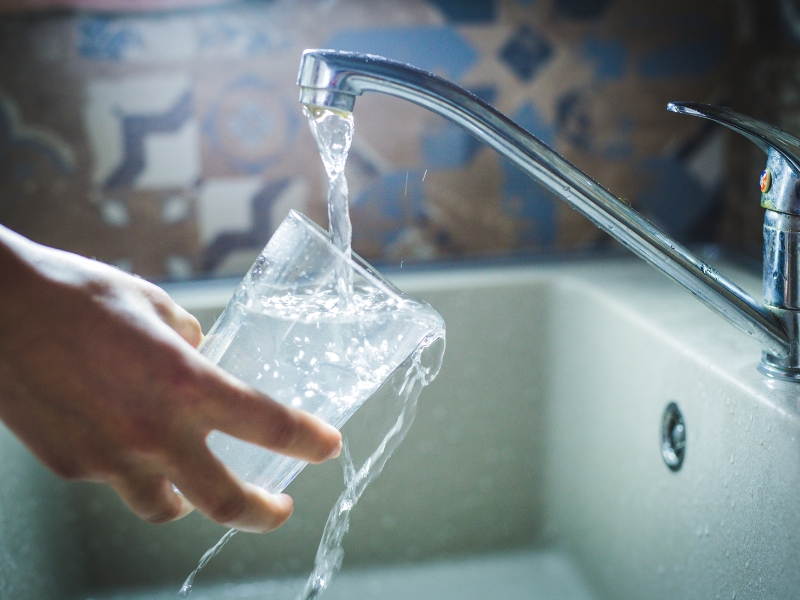Person filling a glass at the sink to drink filtered water.