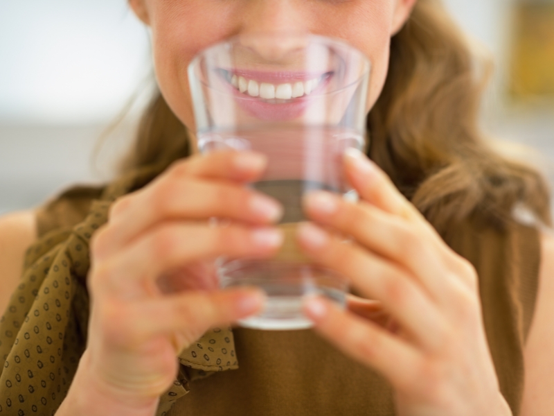 Smiling woman about to drink filtered water from a clear glass.