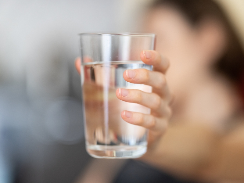 Hand offering a clear glass of filtered water to drink.